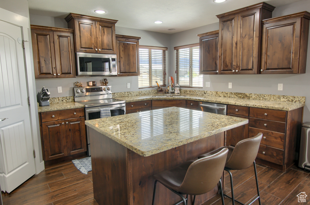 Kitchen featuring a sink, a breakfast bar area, stainless steel appliances, and dark wood-style flooring