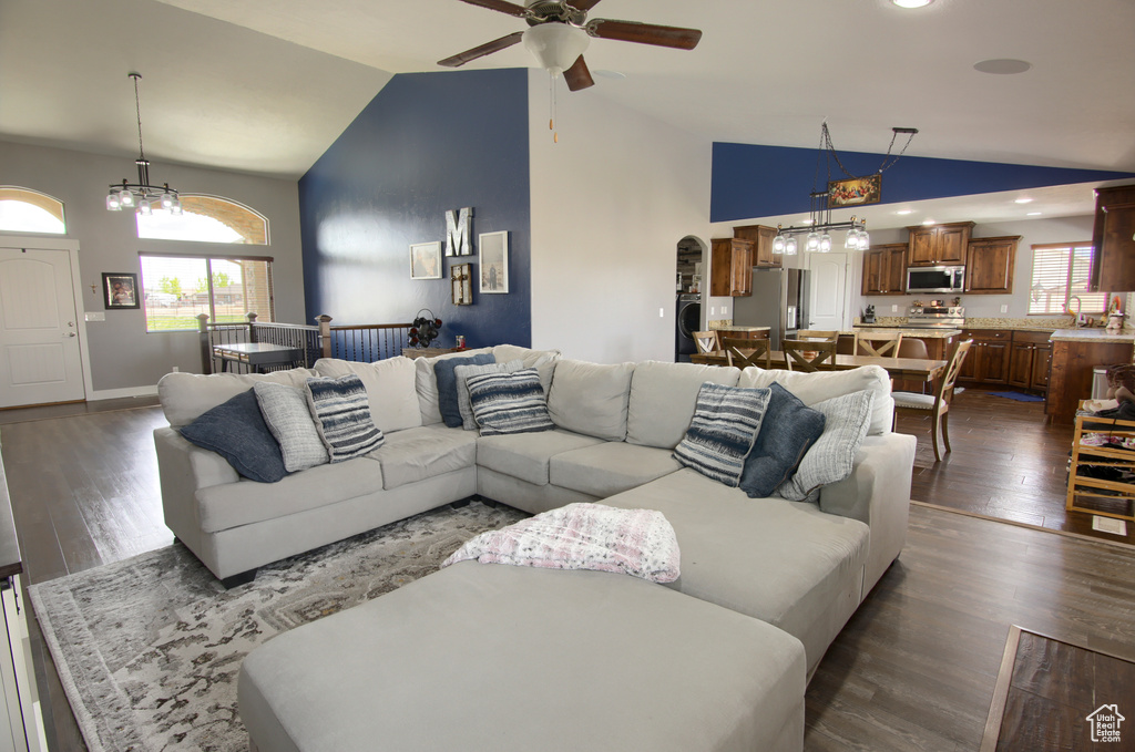 Living room with ceiling fan with notable chandelier, lofted ceiling, a wealth of natural light, and dark wood-style floors