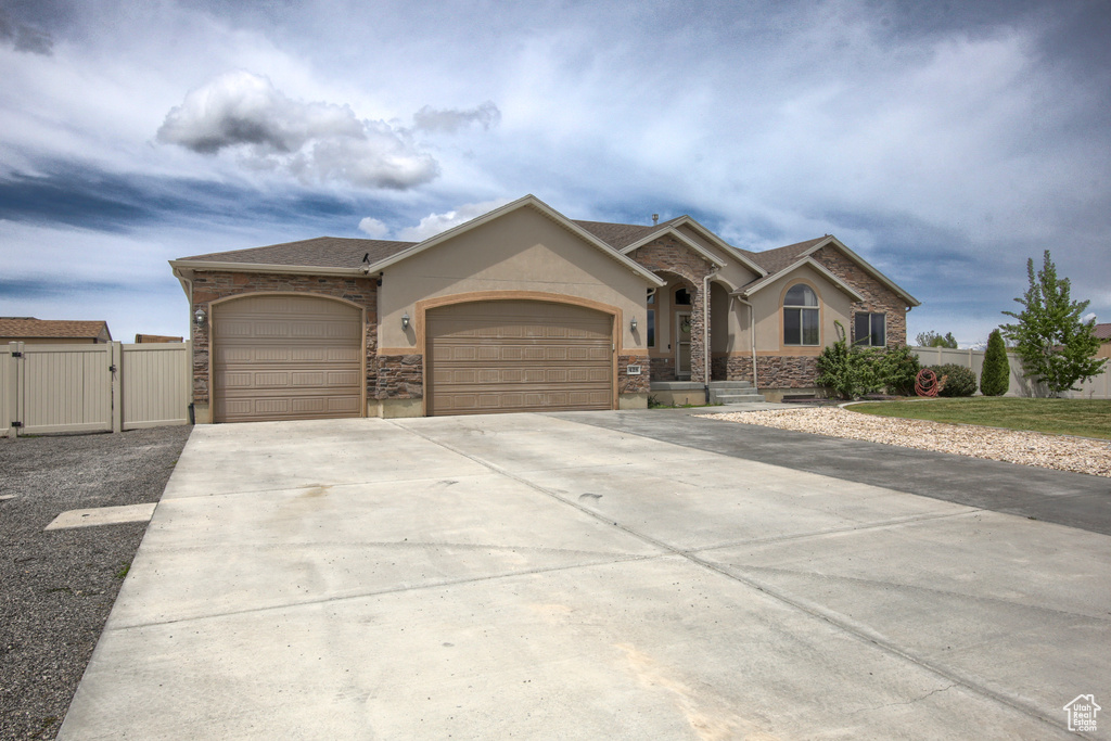 Single story home featuring stucco siding, a gate, stone siding, and a garage