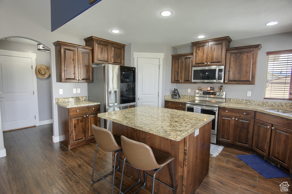 Kitchen with appliances with stainless steel finishes, arched walkways, a kitchen breakfast bar, a center island, and dark wood-type flooring