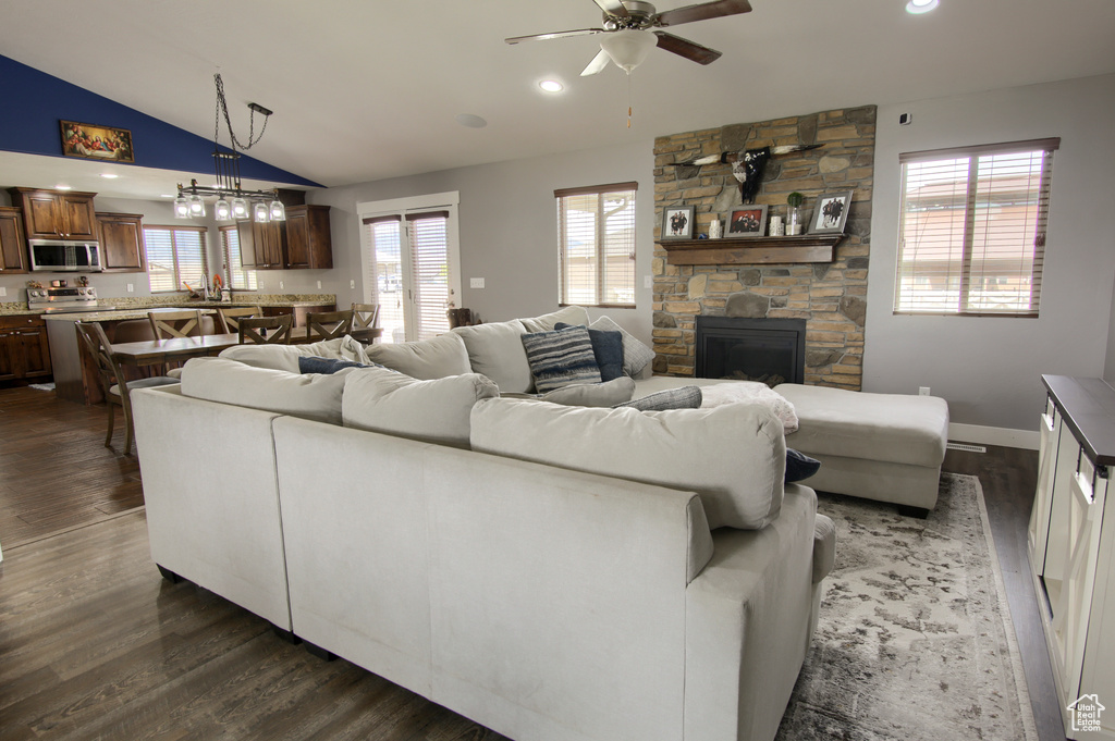 Living area featuring dark wood-style flooring, lofted ceiling, a fireplace, recessed lighting, and ceiling fan with notable chandelier