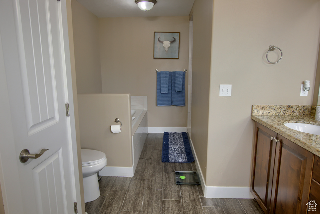 Bathroom featuring vanity, toilet, baseboards, wood finished floors, and a garden tub