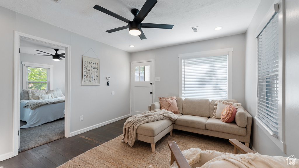 Living room featuring a wealth of natural light, a ceiling fan, visible vents, and dark wood-type flooring