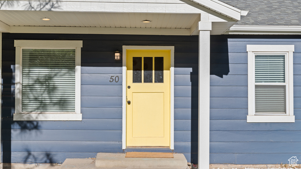 Entrance to property featuring covered porch and a shingled roof