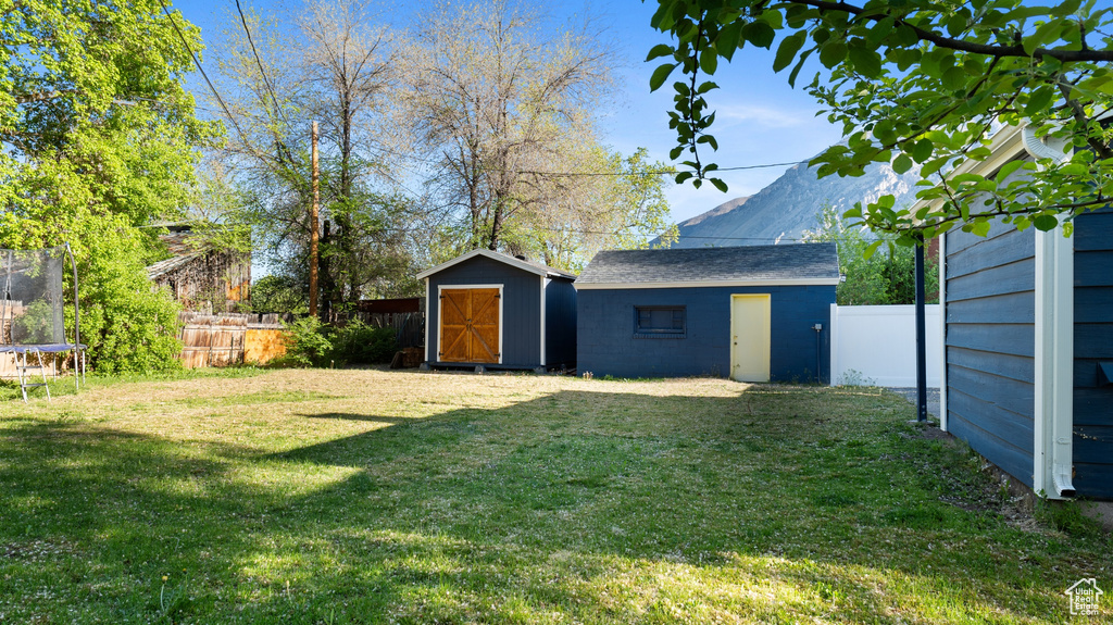 View of yard with a fenced backyard, a storage unit, a trampoline, and an outbuilding