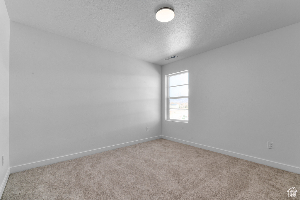 Empty room with baseboards, carpet flooring, a textured ceiling, and visible vents