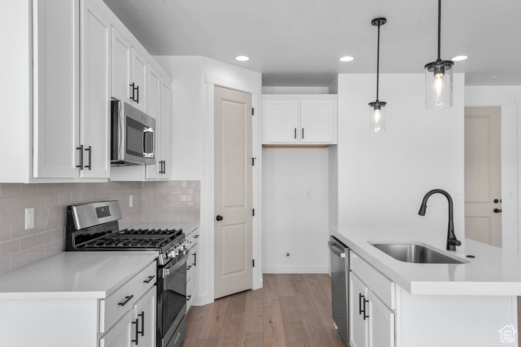 Kitchen with a sink, light wood finished floors, stainless steel appliances, white cabinetry, and decorative backsplash