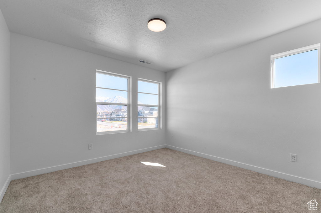 Unfurnished room featuring baseboards, carpet, a textured ceiling, and visible vents