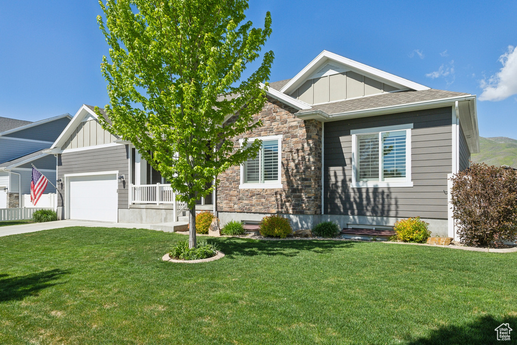 Craftsman inspired home with board and batten siding, stone siding, driveway, a front lawn, and an attached garage