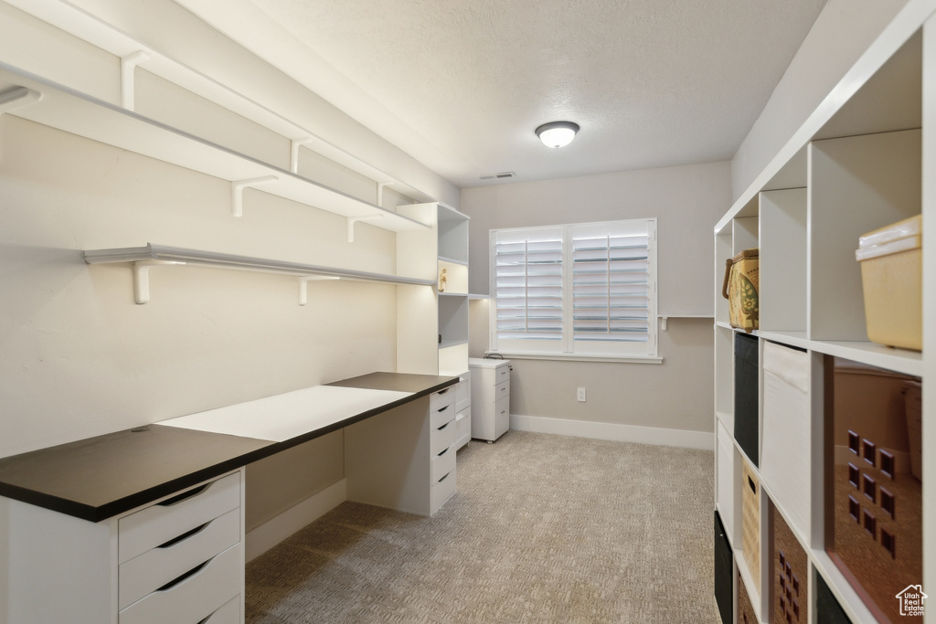 Unfurnished office with carpet floors, built in desk, baseboards, and a textured ceiling