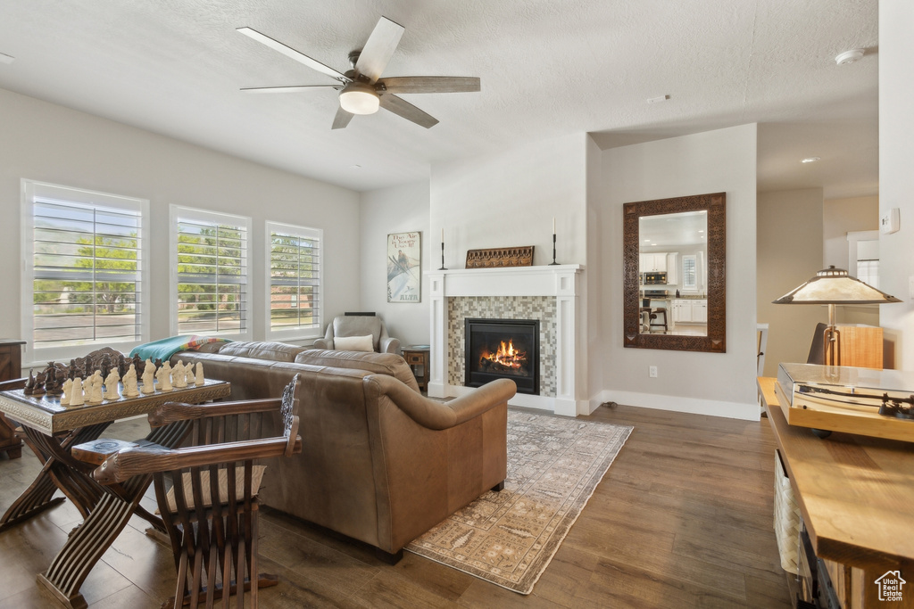 Living area featuring dark wood finished floors, ceiling fan, a tiled fireplace, baseboards, and a textured ceiling