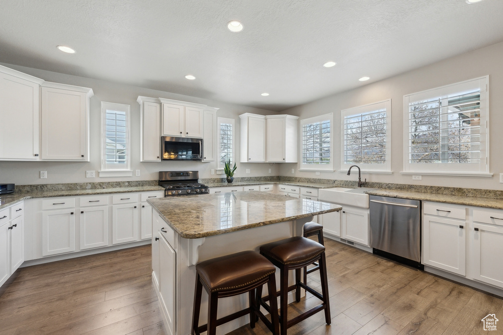 Kitchen featuring a sink, a center island, a breakfast bar, white cabinetry, and appliances with stainless steel finishes