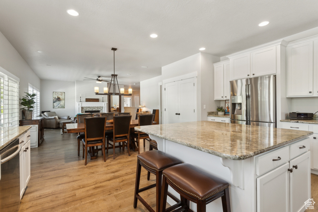 Kitchen with appliances with stainless steel finishes, ceiling fan, a fireplace, light wood-type flooring, and a kitchen island