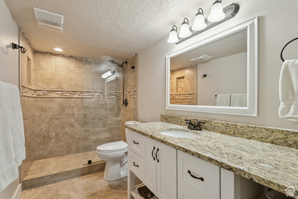 Bathroom featuring vanity, tiled shower, a textured ceiling, and toilet
