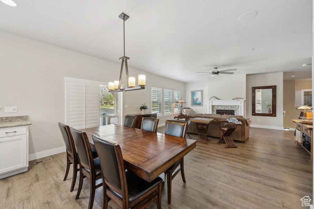 Dining room featuring ceiling fan with notable chandelier, baseboards, a lit fireplace, and light wood-type flooring