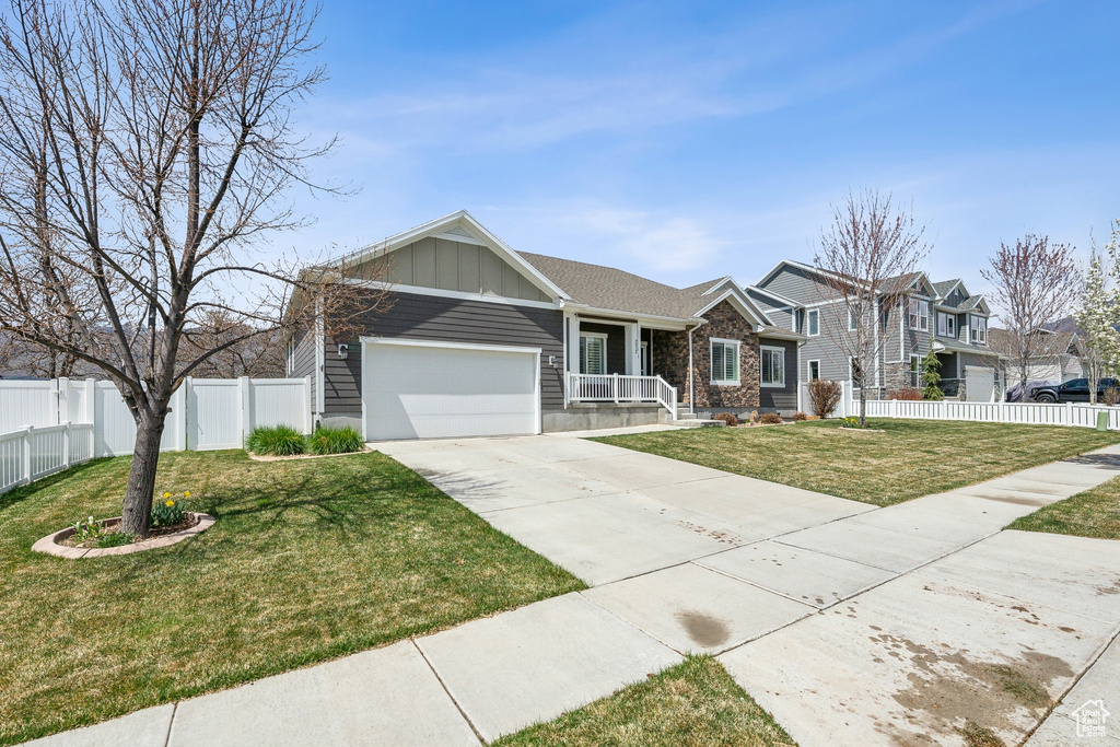 View of front of house with a front lawn, driveway, board and batten siding, an attached garage, and fence