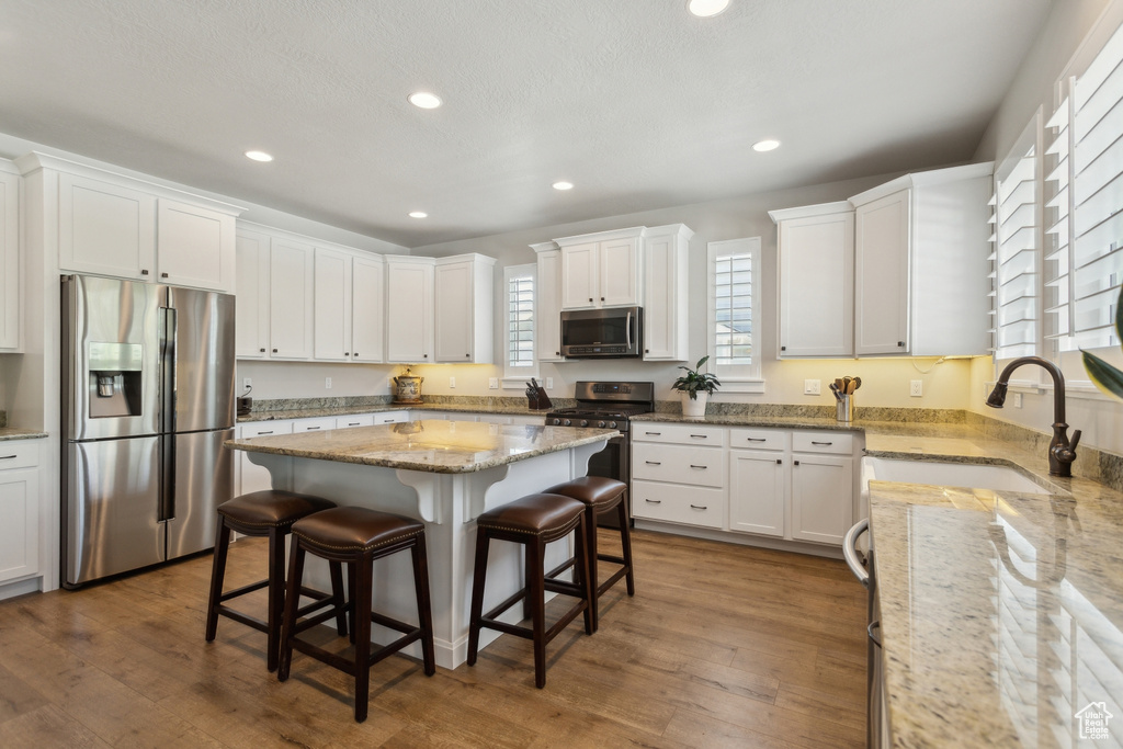 Kitchen with appliances with stainless steel finishes, a sink, a kitchen bar, recessed lighting, and white cabinets