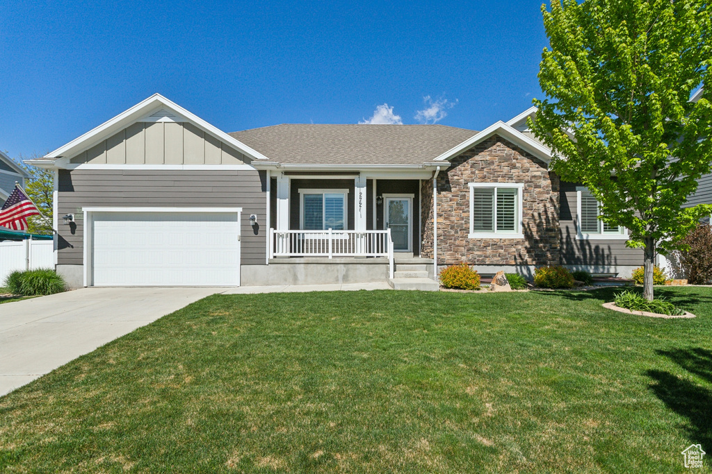 View of front of home with covered porch, a front lawn, concrete driveway, a garage, and stone siding
