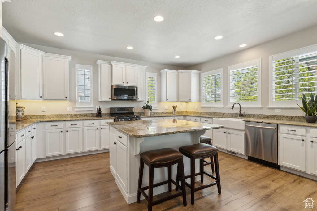 Kitchen featuring stainless steel appliances, a sink, white cabinetry, recessed lighting, and a breakfast bar area