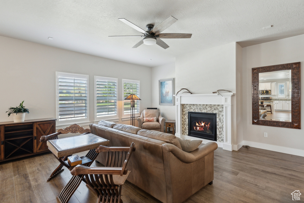 Living room with wood finished floors, a fireplace, baseboards, a ceiling fan, and a textured ceiling