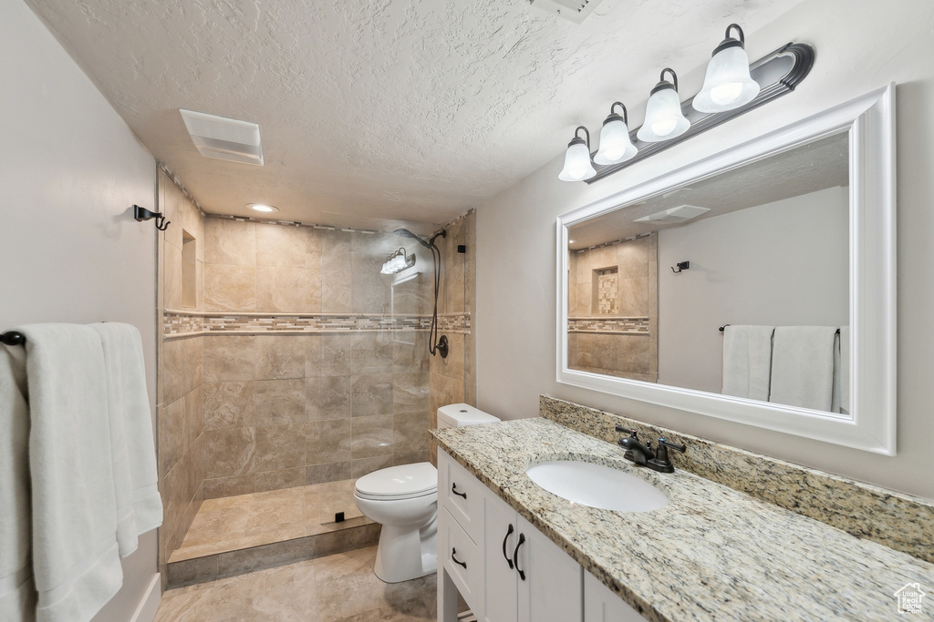 Bathroom featuring vanity, toilet, a tile shower, visible vents, and a textured ceiling