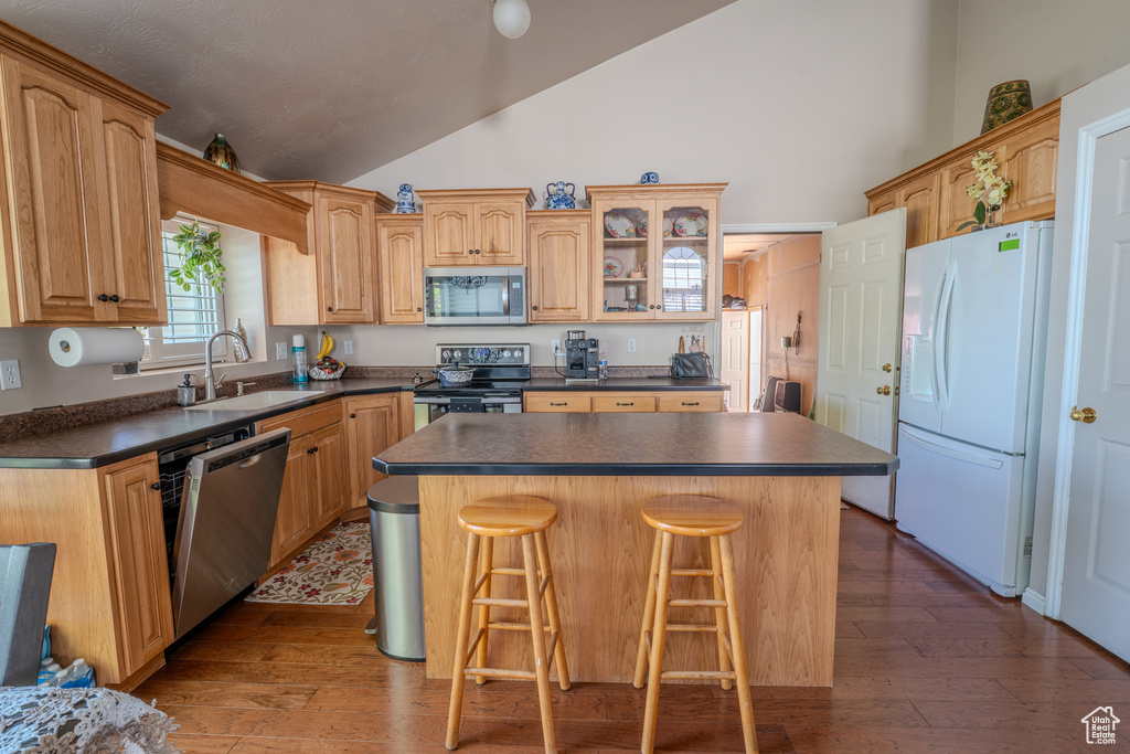 Kitchen with a breakfast bar area, dark countertops, a center island, a sink, and stainless steel appliances