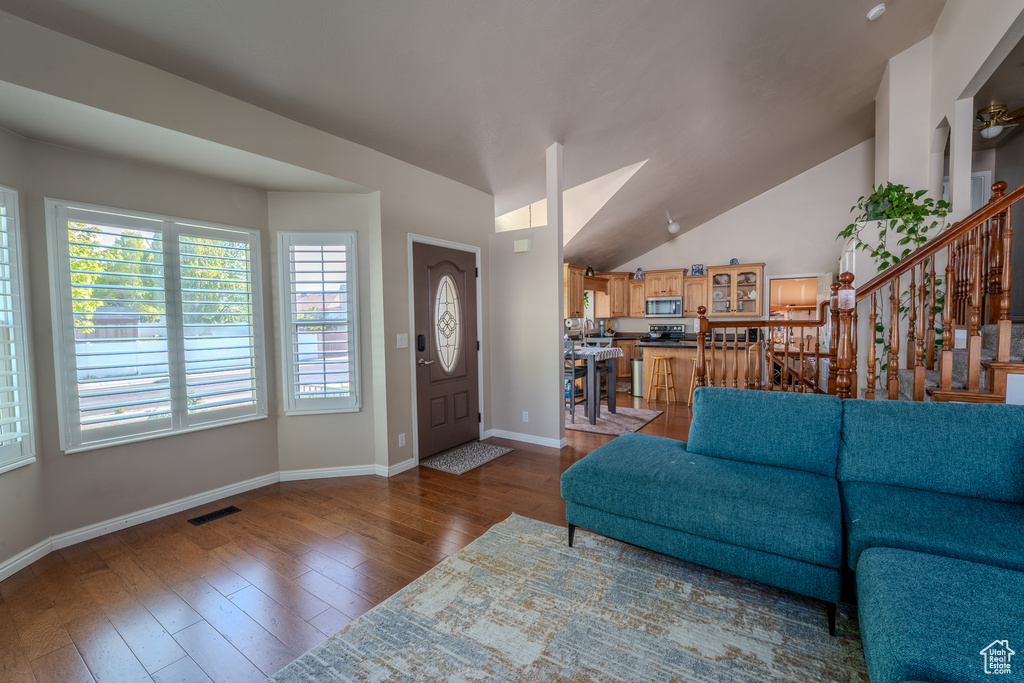 Living room featuring hardwood / wood-style floors, baseboards, vaulted ceiling, visible vents, and stairway