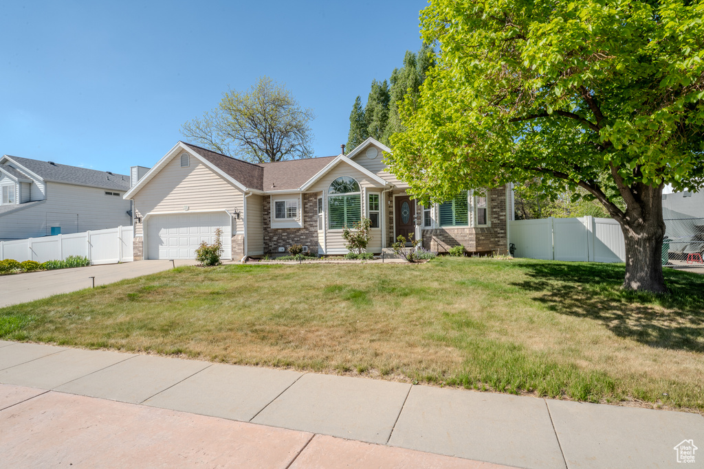 Single story home featuring fence, an attached garage, a front lawn, stone siding, and driveway