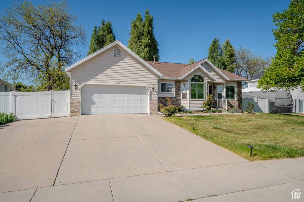 View of front of property featuring a front yard, a gate, fence, concrete driveway, and an attached garage