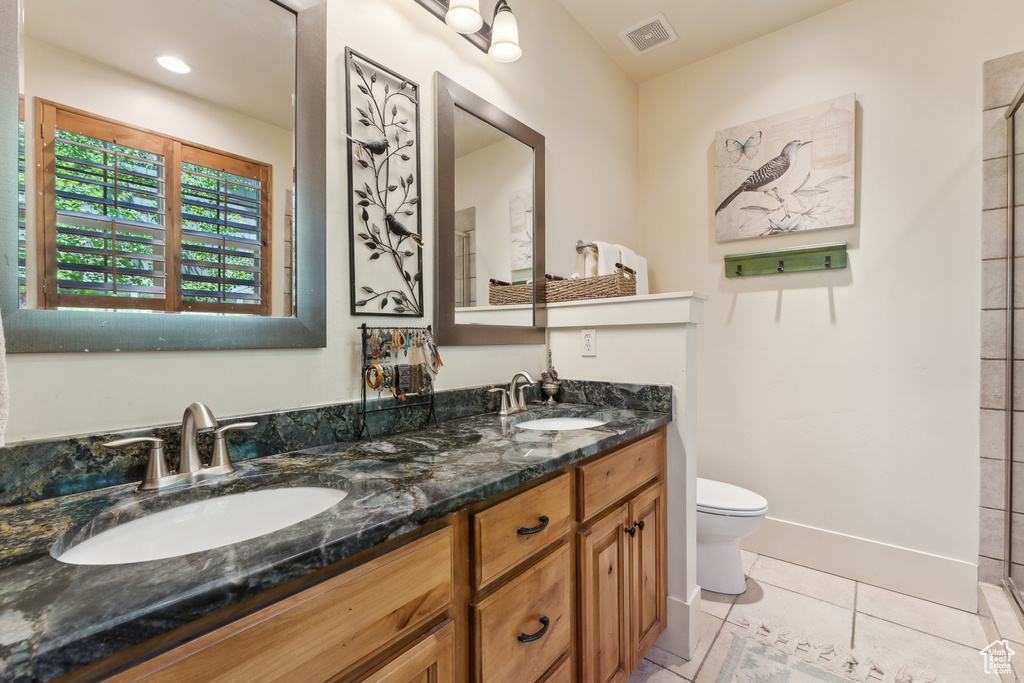 Bathroom featuring toilet, double vanity, tile patterned floors, and baseboards