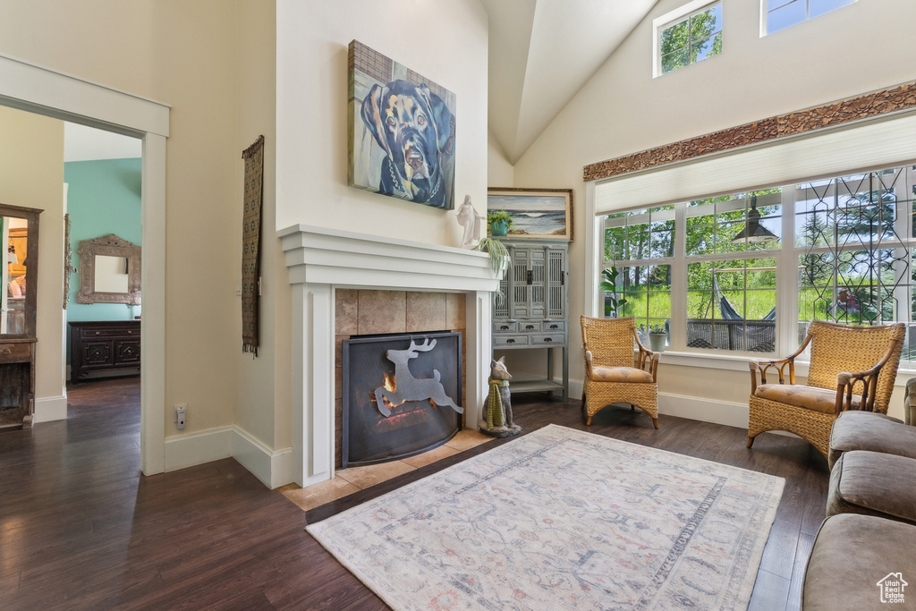 Living area with a tiled fireplace, plenty of natural light, wood finished floors, and high vaulted ceiling