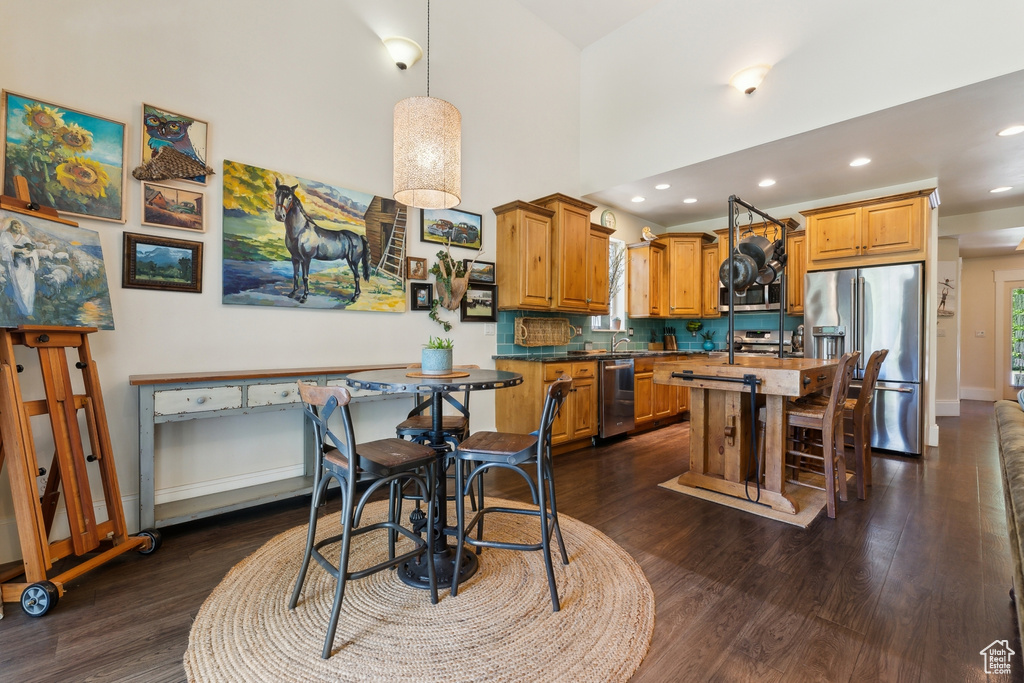 Kitchen with stainless steel appliances, dark wood finished floors, baseboards, an island with sink, and recessed lighting