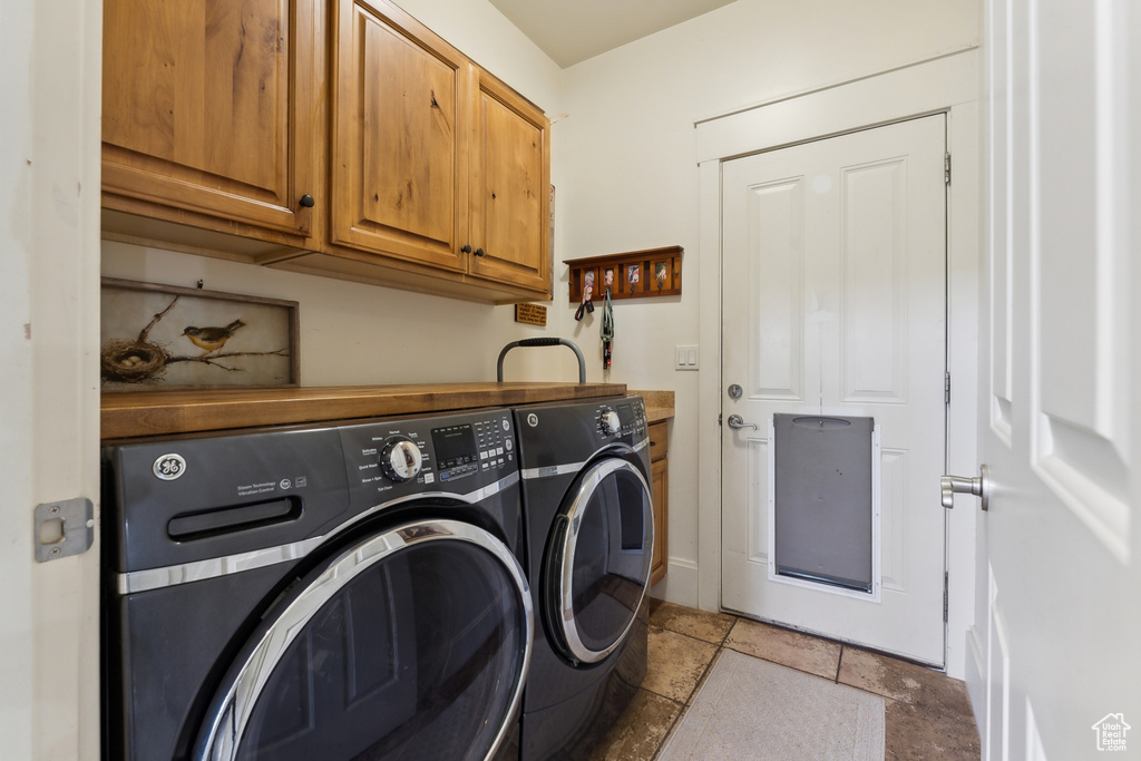 Laundry area featuring cabinet space, separate washer and dryer, stone tile flooring, and baseboards