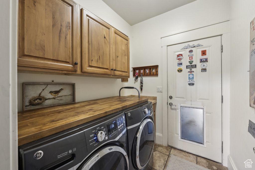 Clothes washing area with baseboards, cabinet space, stone finish floor, and washing machine and clothes dryer