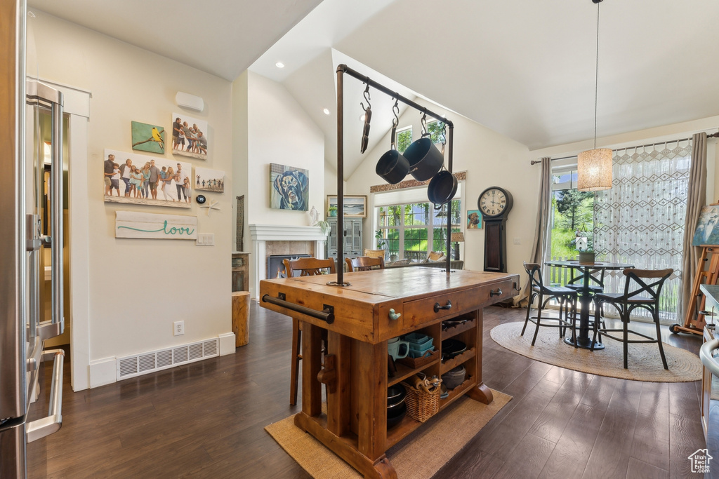 Dining room featuring lofted ceiling, dark wood-style floors, a tiled fireplace, recessed lighting, and baseboards