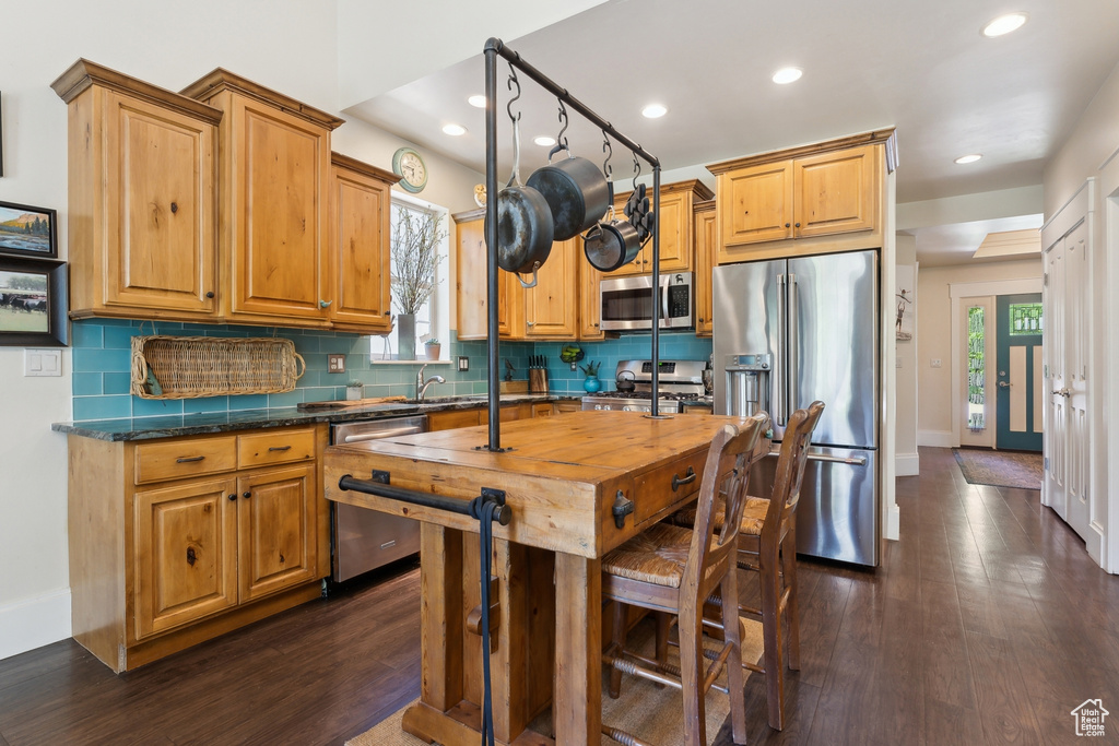 Kitchen with stainless steel appliances, dark wood-style floors, decorative backsplash, recessed lighting, and baseboards
