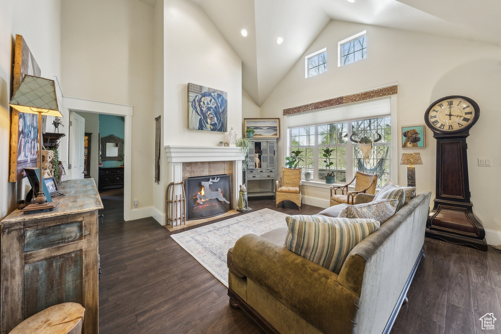 Living room featuring a tiled fireplace, high vaulted ceiling, baseboards, recessed lighting, and dark wood-type flooring