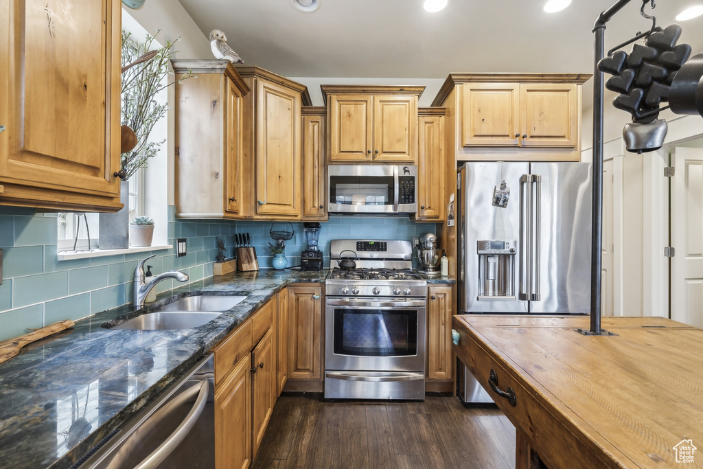 Kitchen with appliances with stainless steel finishes, a sink, dark wood finished floors, dark stone countertops, and tasteful backsplash