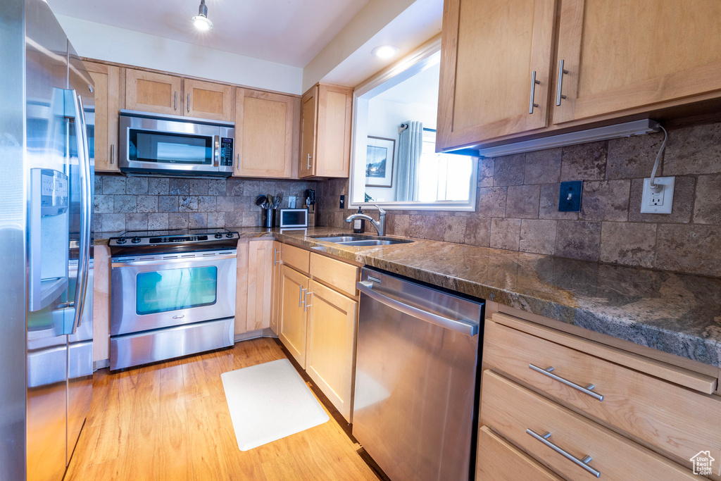 Kitchen with light brown cabinetry, light wood-style floors, appliances with stainless steel finishes, backsplash, and a sink