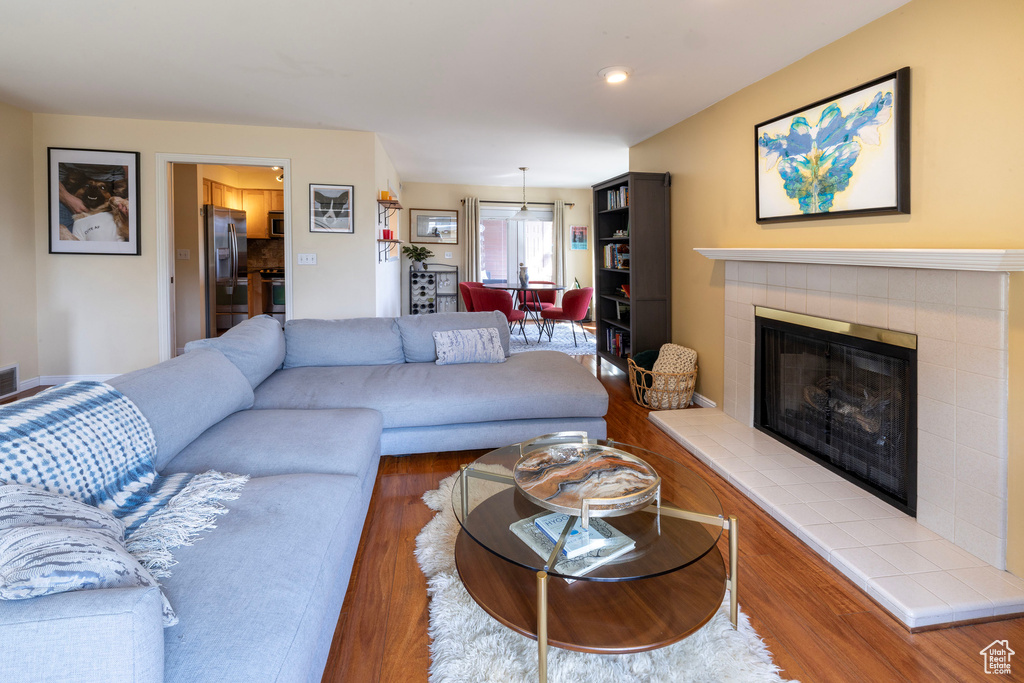 Living room with a tiled fireplace, visible vents, and wood finished floors