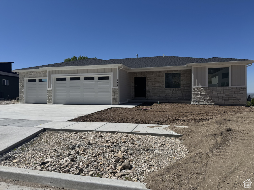 Single story home with roof with shingles, stone siding, a garage, board and batten siding, and concrete driveway