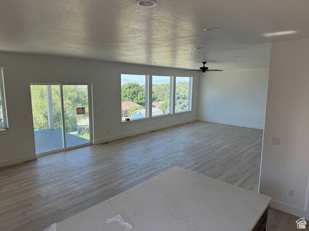 Unfurnished living room featuring baseboards, ceiling fan, a textured ceiling, and wood finished floors