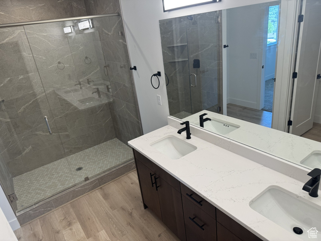 Full bathroom with a sink, double vanity, a shower stall, and wood finished floors