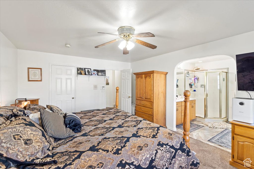 Bedroom featuring a ceiling fan, arched walkways, ensuite bath, and light carpet
