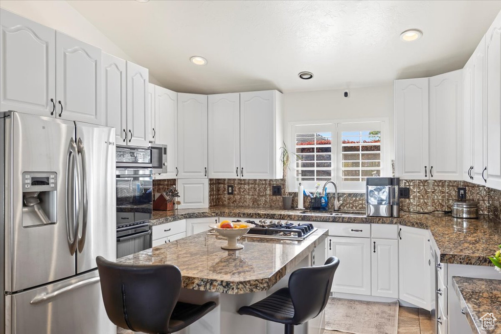 Kitchen with decorative backsplash, a kitchen breakfast bar, a sink, white cabinets, and stainless steel appliances