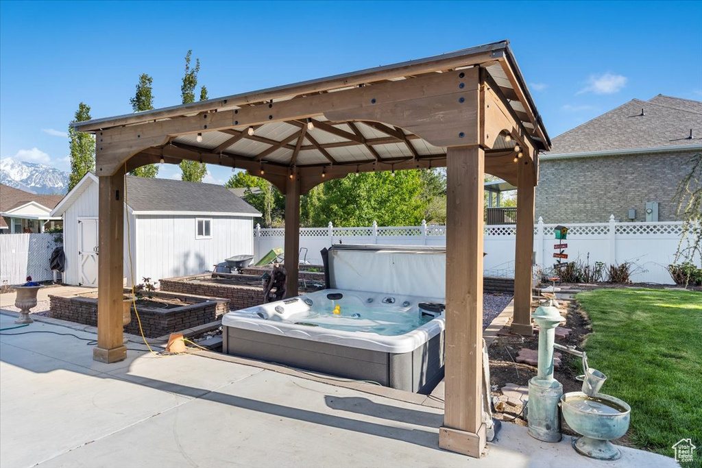 View of patio / terrace featuring a gazebo, a fenced backyard, a hot tub, and an outdoor structure