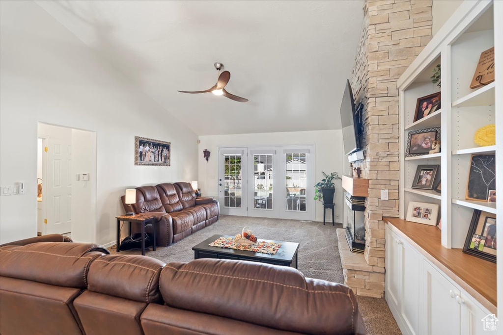 Living area with a stone fireplace, a ceiling fan, high vaulted ceiling, and light carpet