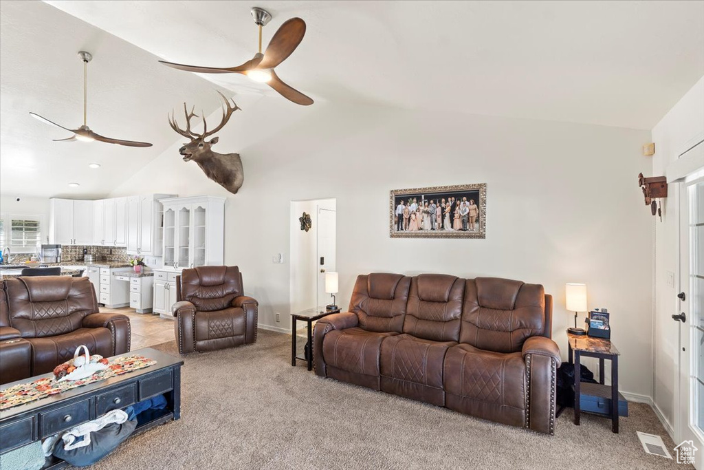 Living room with a ceiling fan, visible vents, baseboards, lofted ceiling, and light carpet