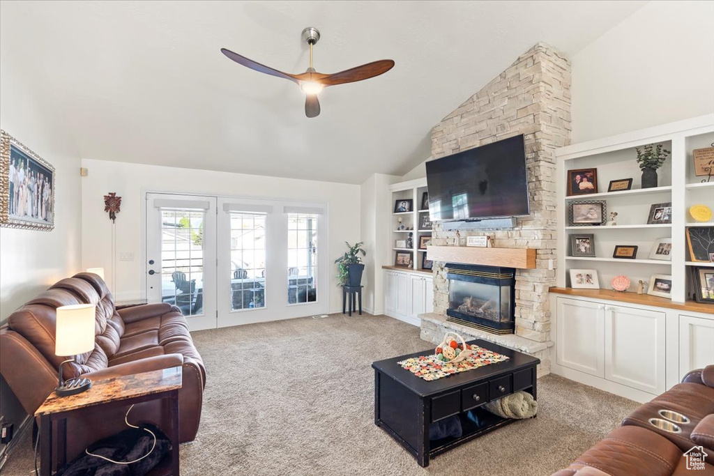 Living area featuring a ceiling fan, light colored carpet, a stone fireplace, and lofted ceiling