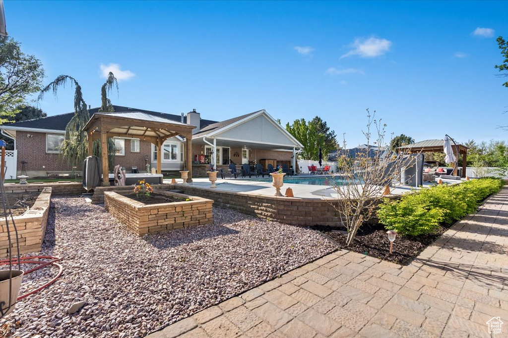 Rear view of property with a gazebo, an outdoor pool, a patio area, and brick siding